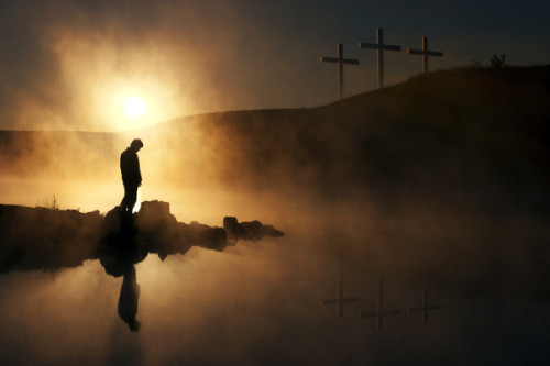 Three Crosses and Silhoutted Person in Prayer at Sunrise